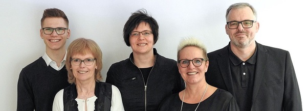 Fünfköpfiges Team mit Brille und Business-Kleidung vor weißem Hintergrund, Gruppenfoto.