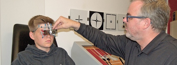 Ein Optiker führt bei einem Jungen mit Spezialgerät einen Sehtest zur Augenvermessung durch.